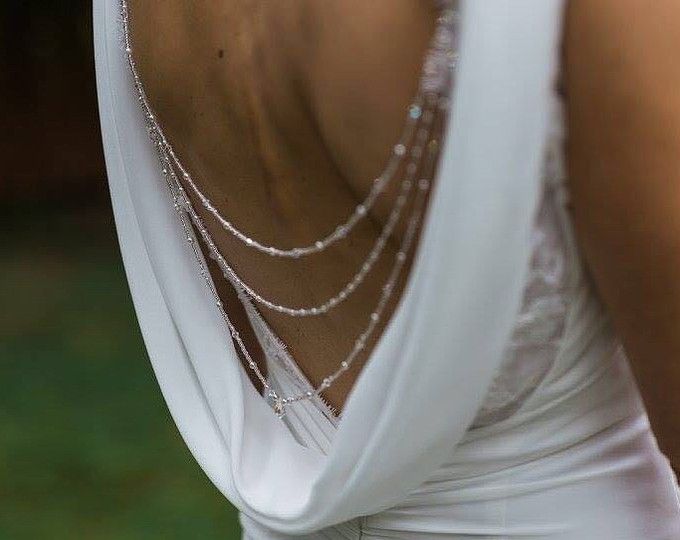 the back of a woman's white dress with silver chains on her neck and shoulders