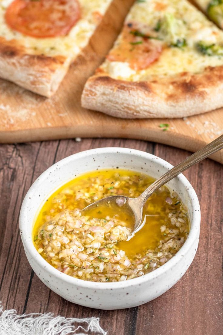 a white bowl filled with soup sitting on top of a wooden table next to slices of pizza