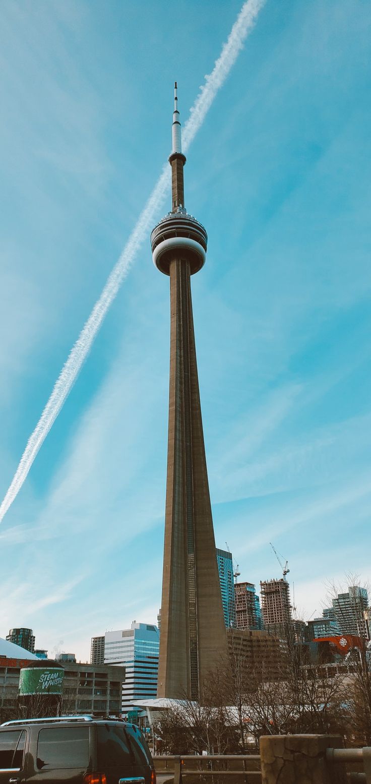 a tall tower with a sky scraper in the background and cars parked below it