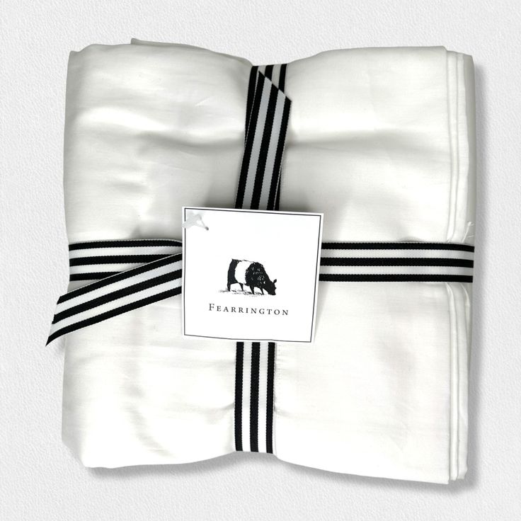 A neatly folded white fabric from the Fearrington Lifestyle Bedding Collection - Frette Queen Flat Sheet is tied with a black and white striped ribbon. A tag attached to the ribbon features a small black silhouette of a cow with "Fearrington" below it Pet Holiday, Gifted Kids, Fashion Accessories Jewelry, Bedding Collections, Flat Sheets, Apparel Accessories, Fashion Accessories, Lifestyle, Queen