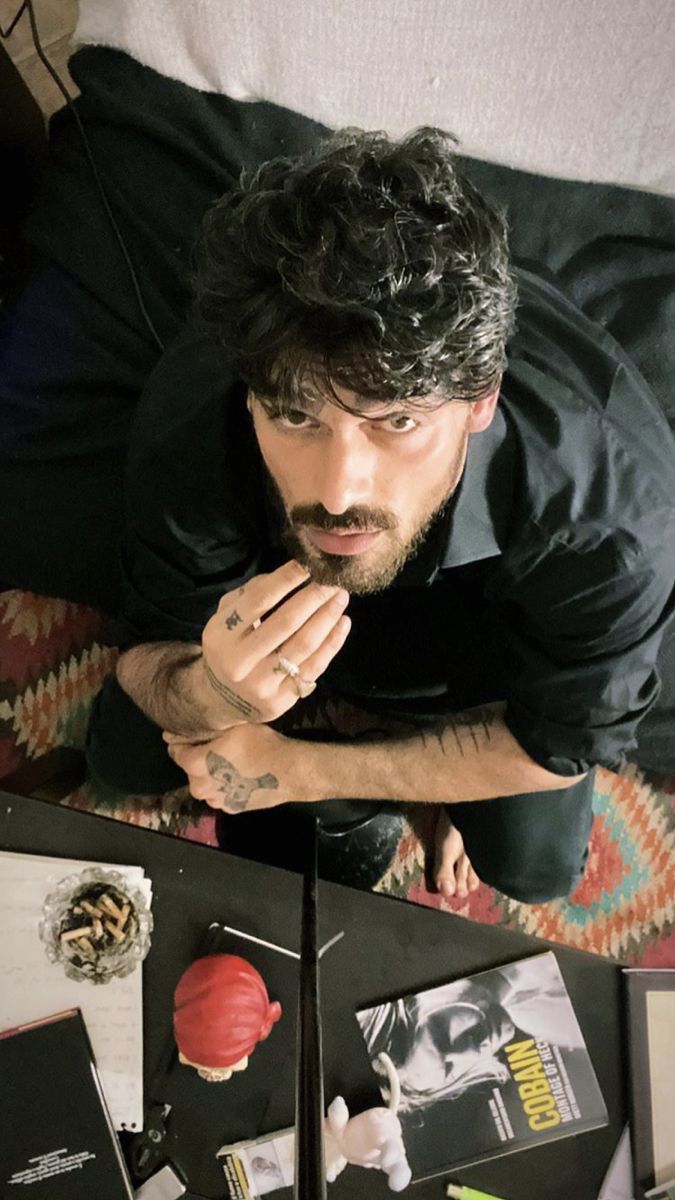 a man sitting on top of a bed next to a table filled with books and other items