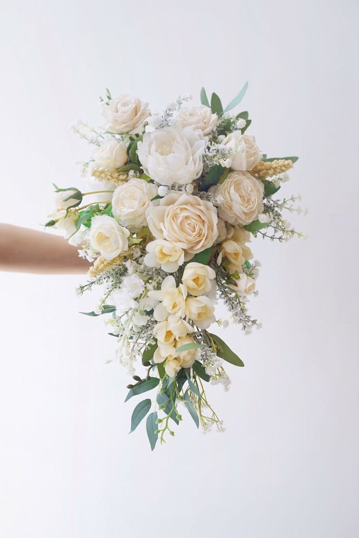 a bridal bouquet being held up by someone's hand in front of a white wall