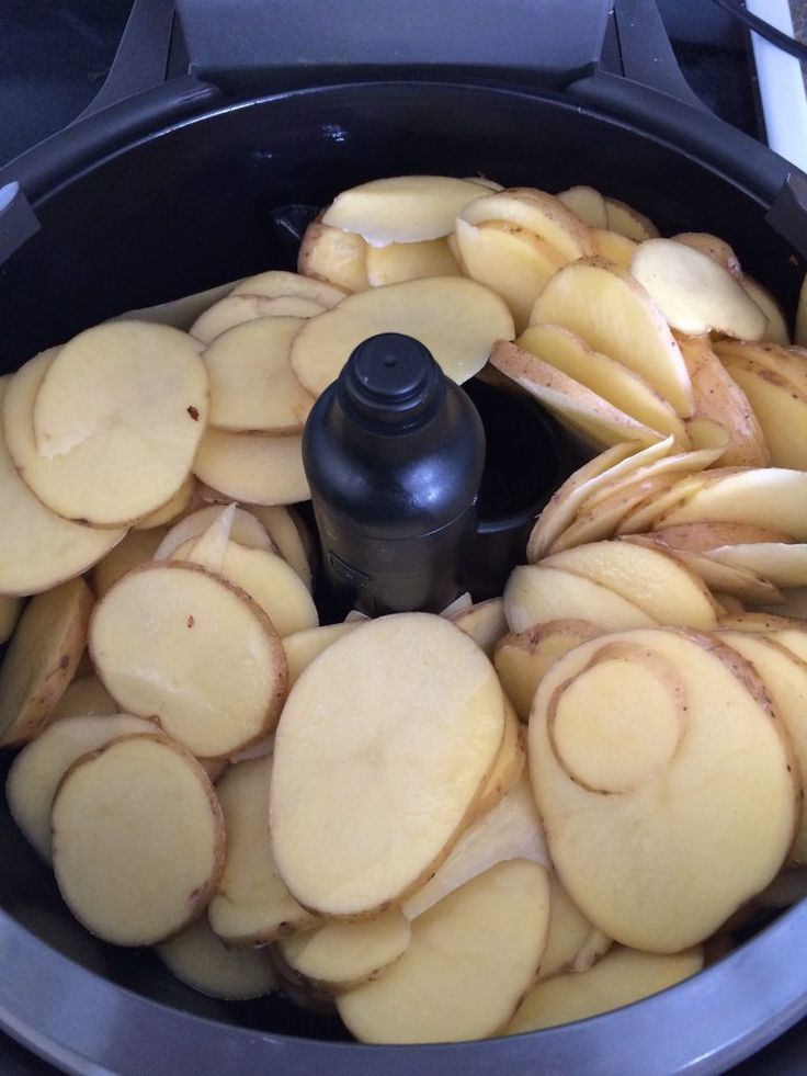 sliced potatoes are being cooked in an air frying pan with a black bottle on top