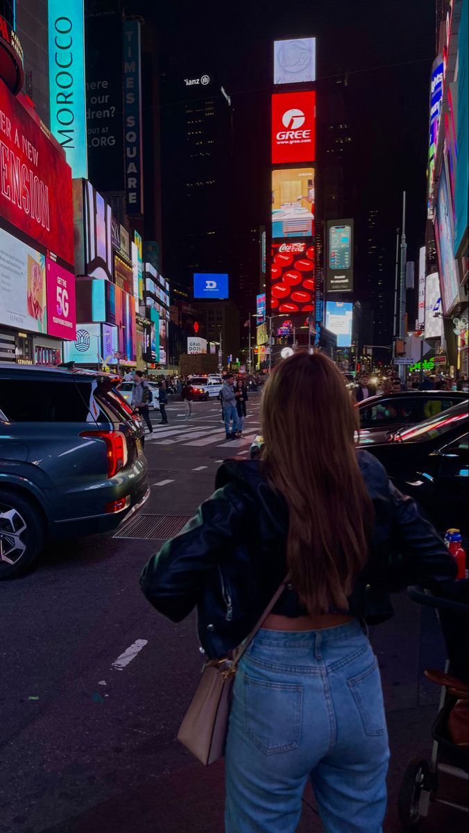 a woman is walking down the street in times square, new york city at night