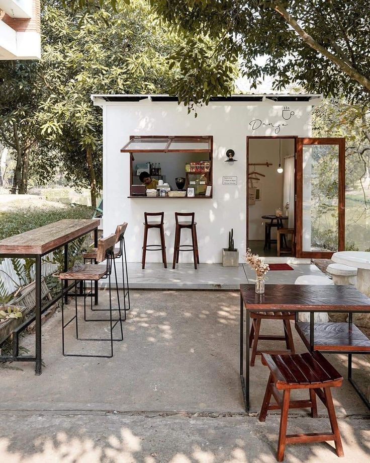 an outdoor dining area with wooden tables and stools next to a small white building