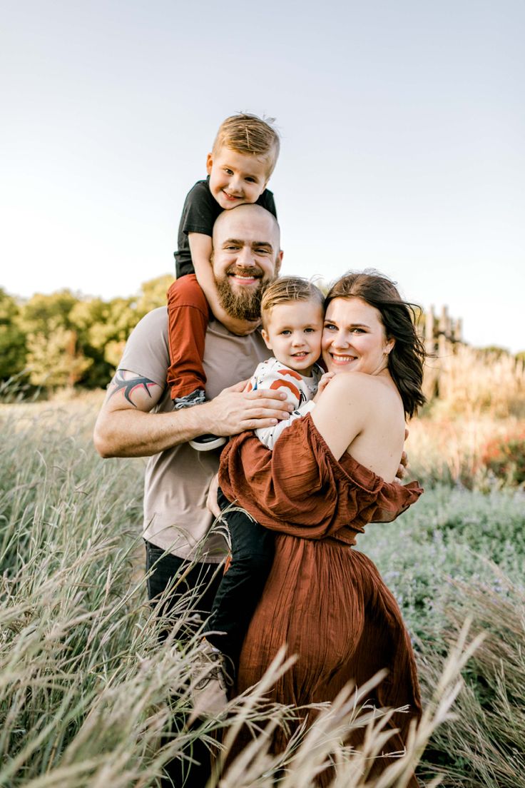 a man, woman and child are posing for a photo in the tall grass with their arms around each other