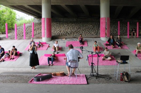 a group of people sitting on pink mats in front of an overpass with music instruments