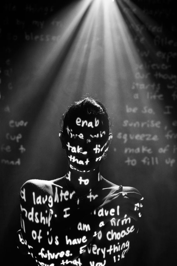 a man with words written all over his body in front of a light that is shining down on him