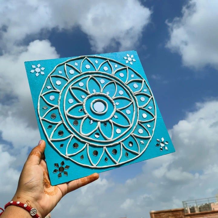 a hand holding up a blue paper cutout that looks like a circular flower design