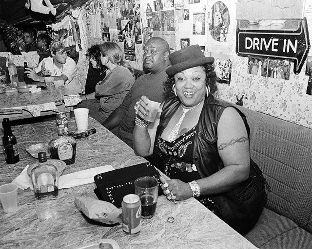 black and white photograph of people sitting at a table in a restaurant with signs on the wall