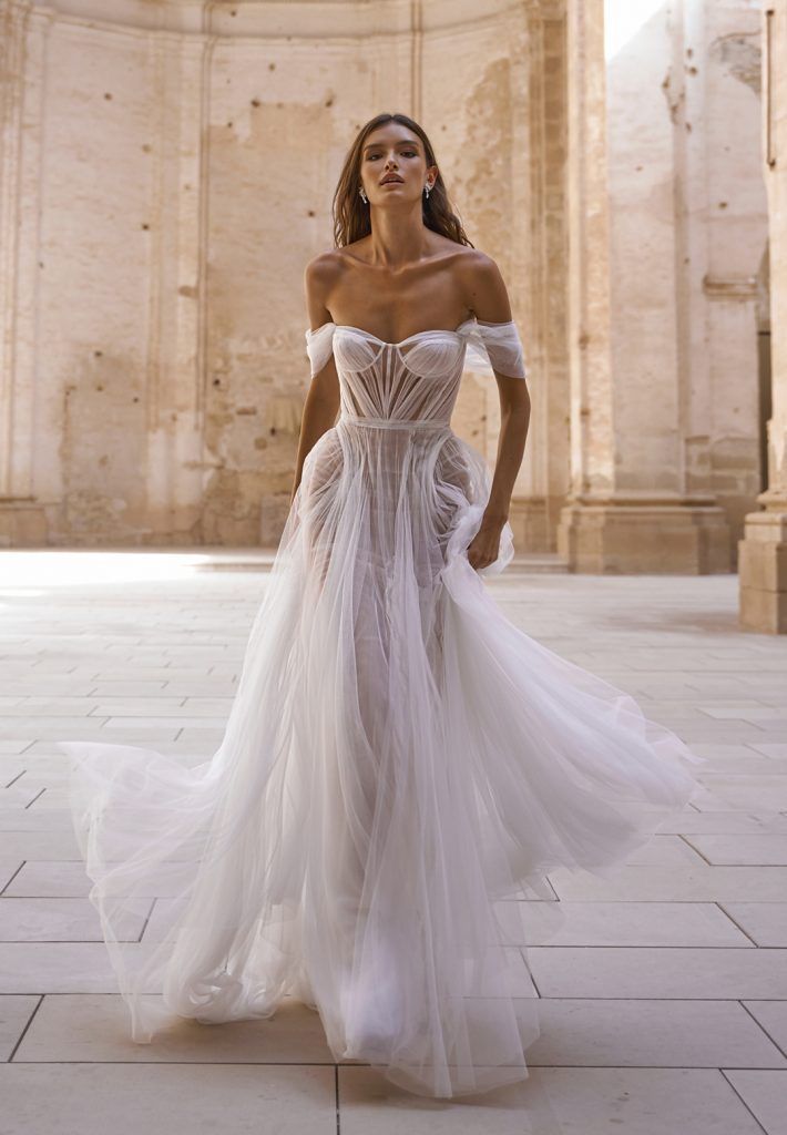 a woman in a white wedding dress standing on the floor with her hands behind her back