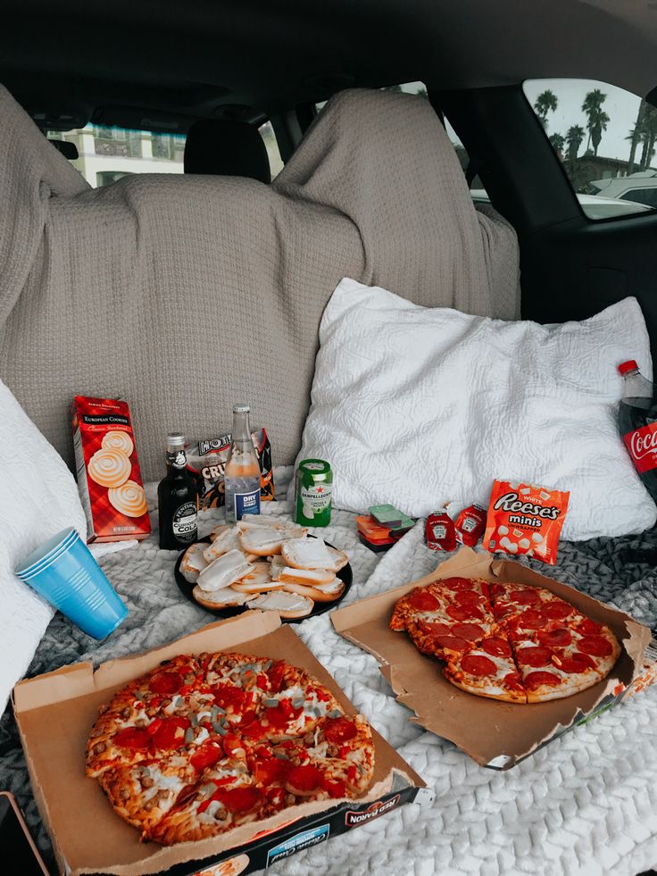 two pizzas are sitting on the back seat of a car with snacks and drinks