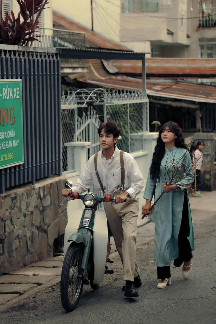 a man and woman riding on the back of a scooter down a street