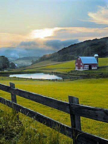 a farm field with a fence and a red barn in the distance on a cloudy day