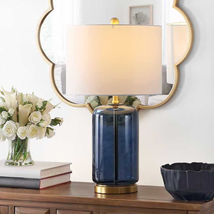 a blue vase with white flowers and a lamp on a table next to a mirror