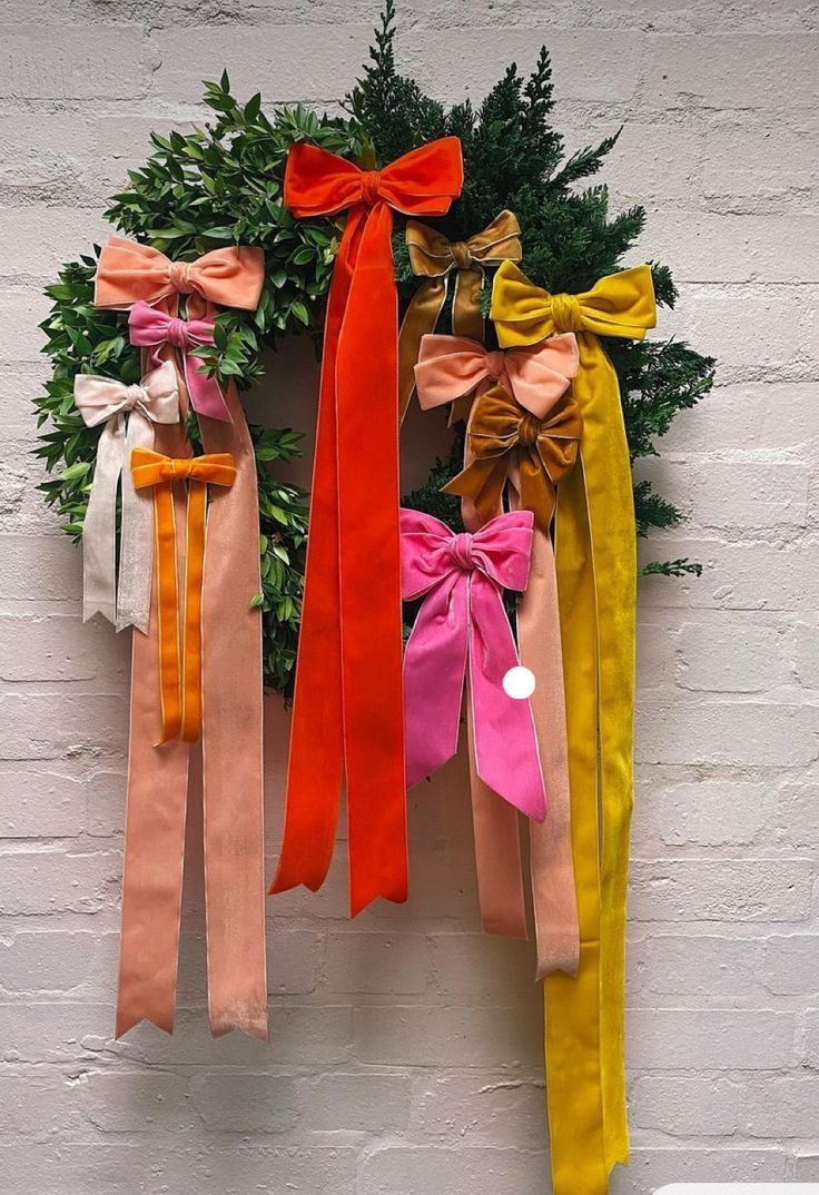 an assortment of bows hanging on a wall next to a wreath with greenery in the background