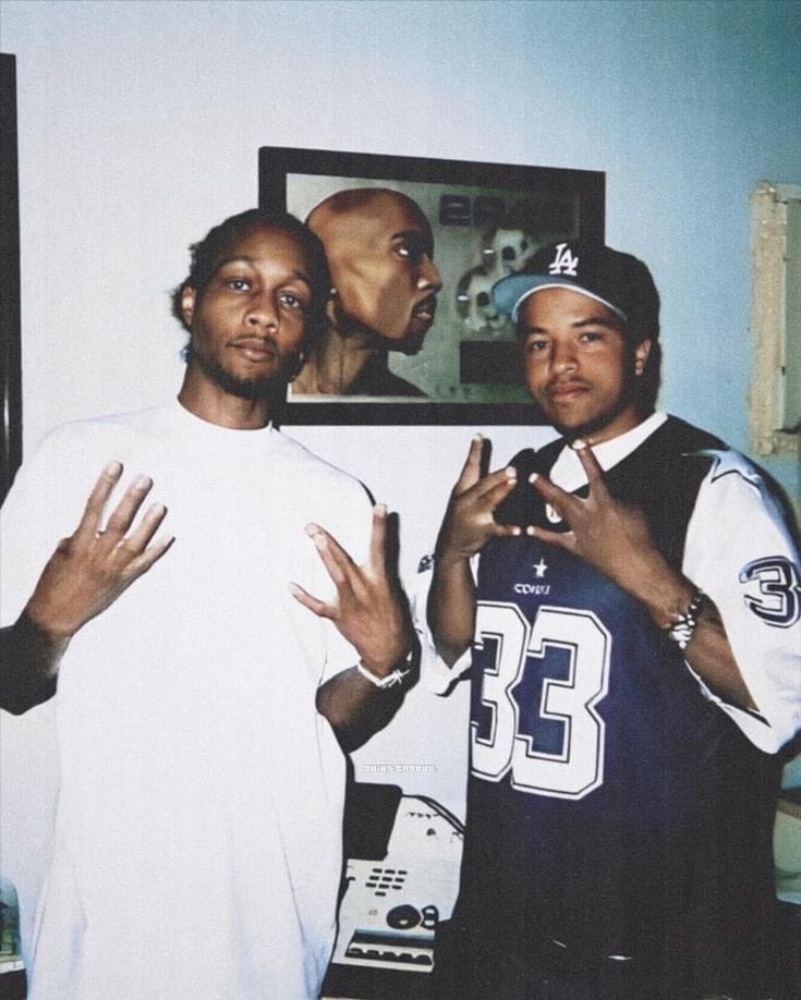 two men standing next to each other in front of a wall with pictures on it