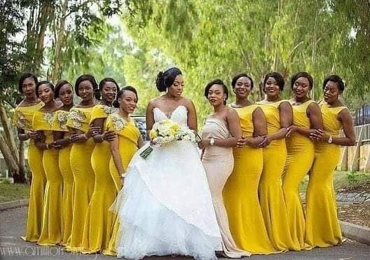 a group of women standing next to each other wearing yellow dresses and holding bouquets