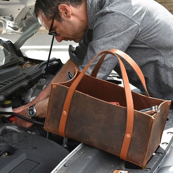 a man working on an engine in the hood of a car with a tool bag