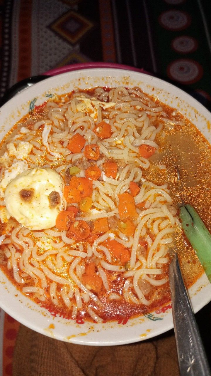 a plate of noodles with carrots and an egg on top next to a pair of tongs