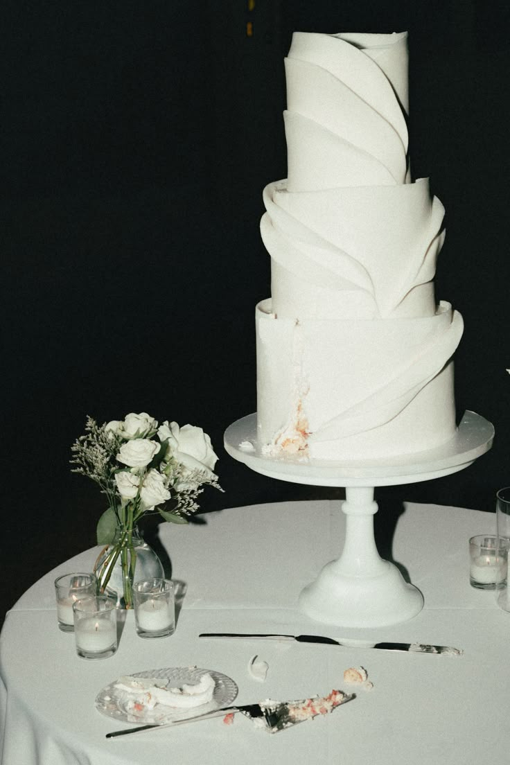 a white wedding cake sitting on top of a table next to some glasses and flowers