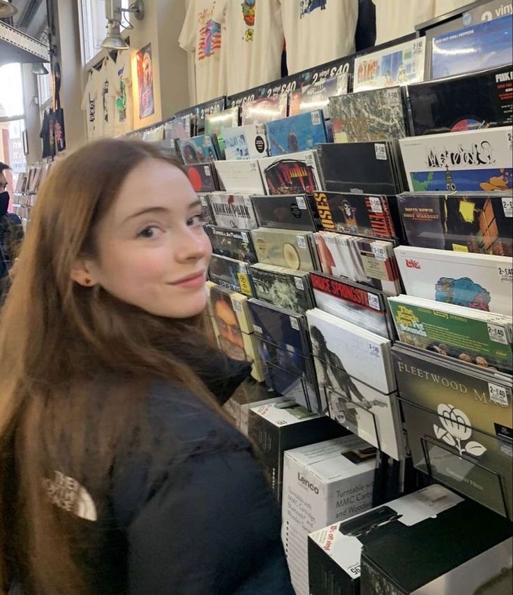 a young woman standing in front of a wall full of cd's and cds