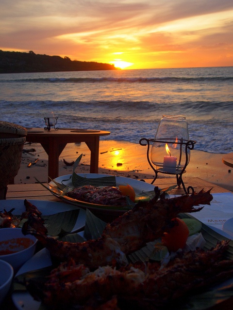 a table with food on it at the beach near the water and sunset in the background