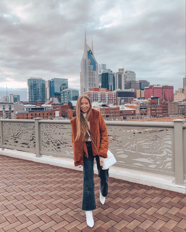 a woman standing on top of a bridge next to a tall building with a city in the background