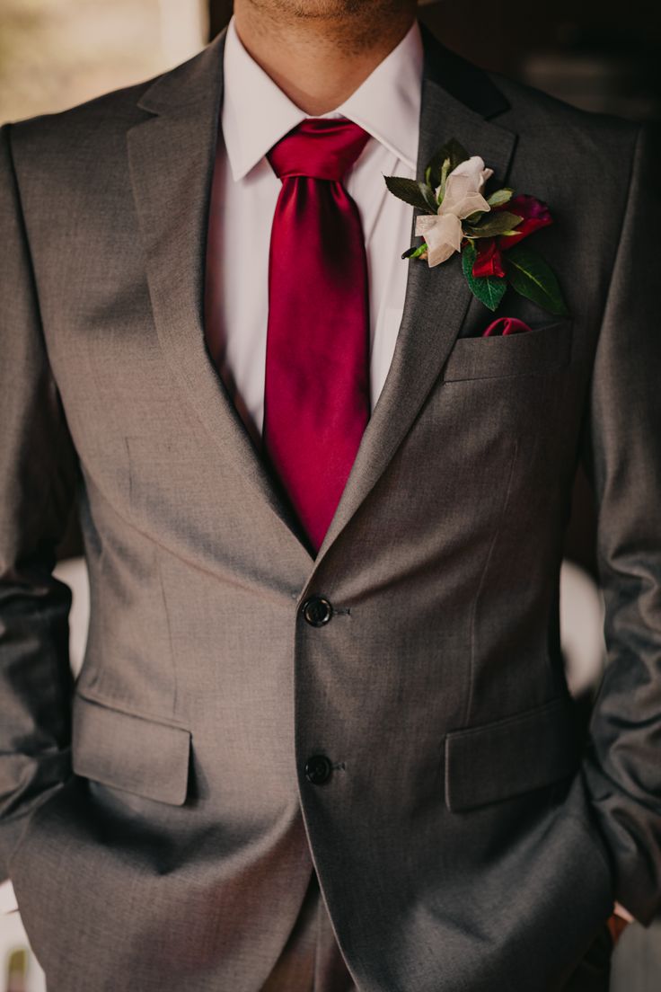 a man in a gray suit with a red tie and flower boutonniere