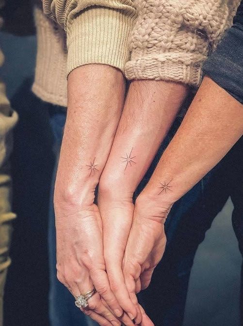 two people holding hands with small stars on their wrist tattooing each other's fingers