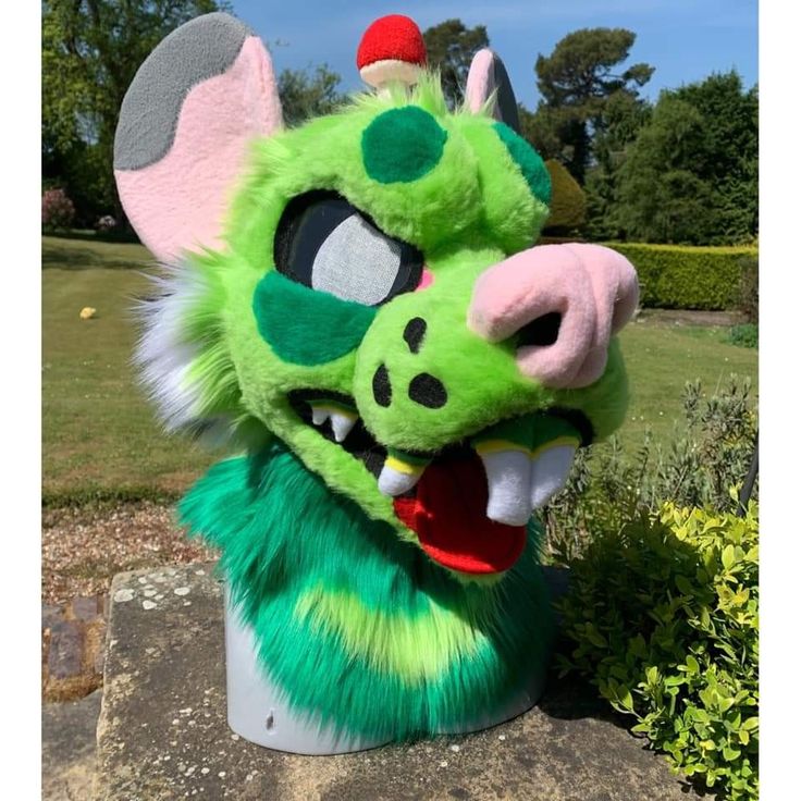 a green and pink dragon mask sitting on top of a rock