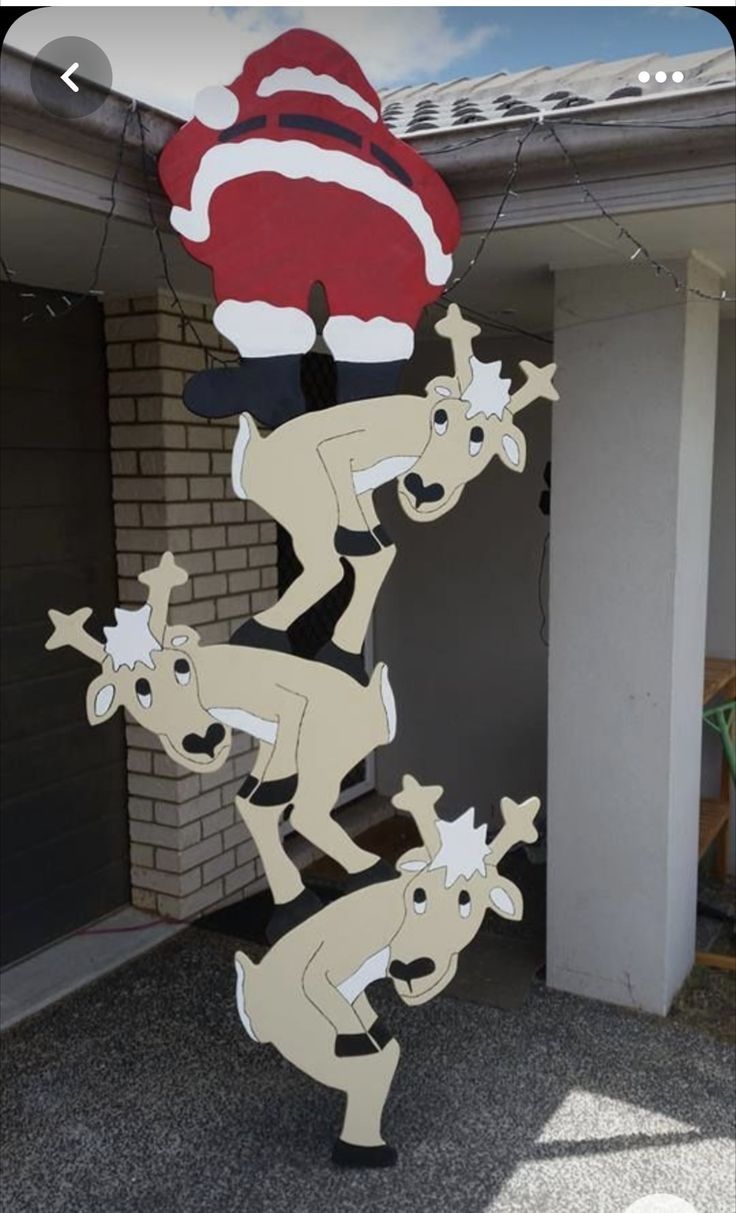 a christmas decoration with santa hats and reindeers on it's head in front of a house