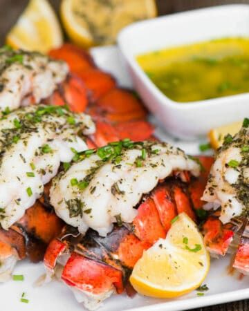 lobster with lemon and parsley garnish on a white plate next to dipping sauce