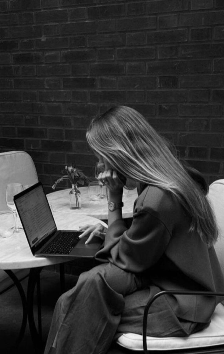 a woman sitting at a table with a laptop computer on her lap while talking on the phone