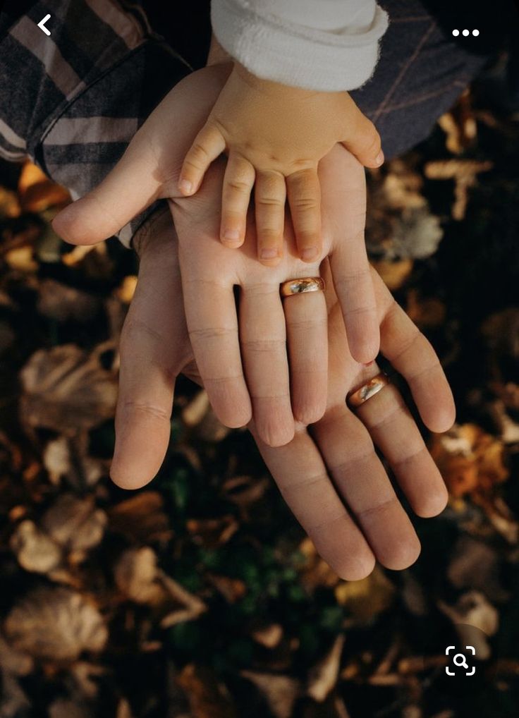 two hands holding each other with wedding rings on their fingers in front of some leaves