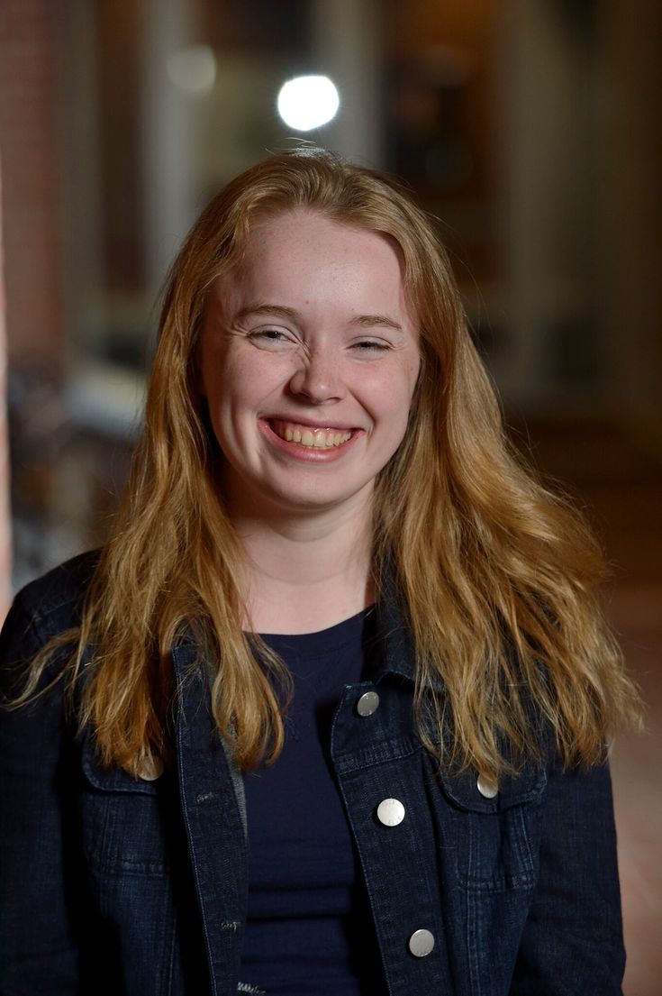 a woman with long blonde hair smiling at the camera while wearing a black jacket and jeans