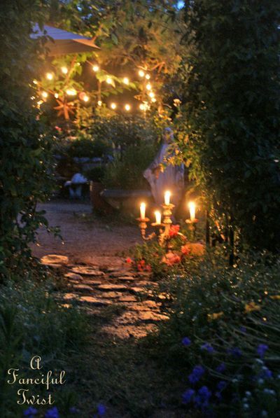 candles are lit in the middle of a garden path at night with flowers and greenery