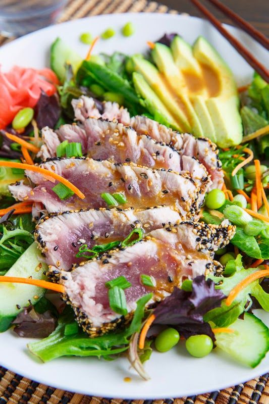 a white plate topped with meat and veggies next to sliced avocado