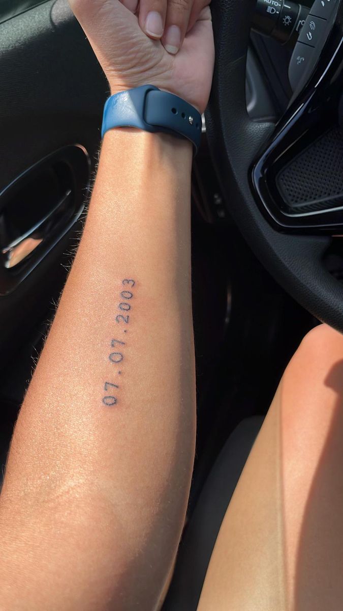 a person with a wrist tattoo on their arm holding the steering wheel of a car