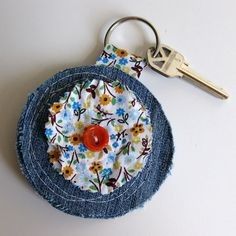 a denim coin purse with a red button and flowered design on the front, sitting on a white surface