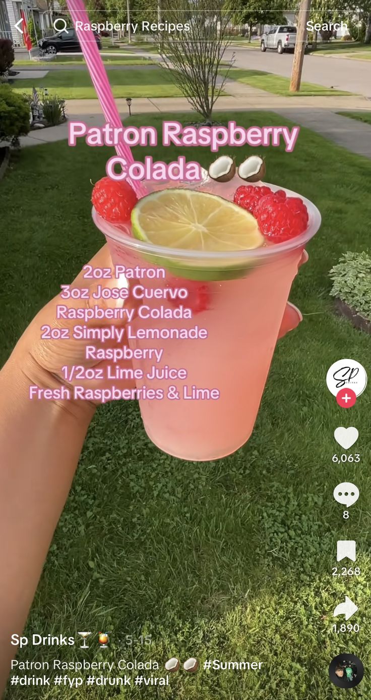 a person holding up a drink with raspberries and lime in it on the grass