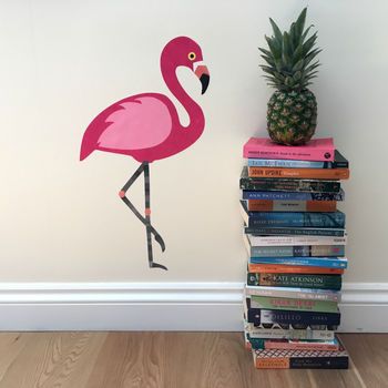 a pink flamingo standing on top of a pile of books next to a pineapple