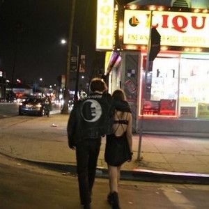 a man and woman walking down the street in front of a liquor store at night