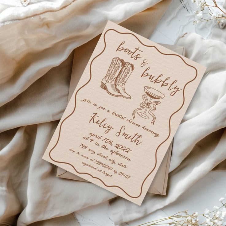 a wedding card with cowboy boots on it sitting on top of a bed covered in white sheets