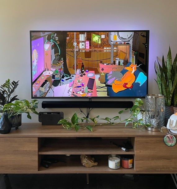 a flat screen tv sitting on top of a wooden entertainment center next to potted plants