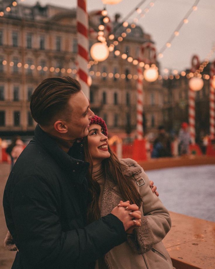 a man and woman embracing each other in front of christmas lights on the water's edge