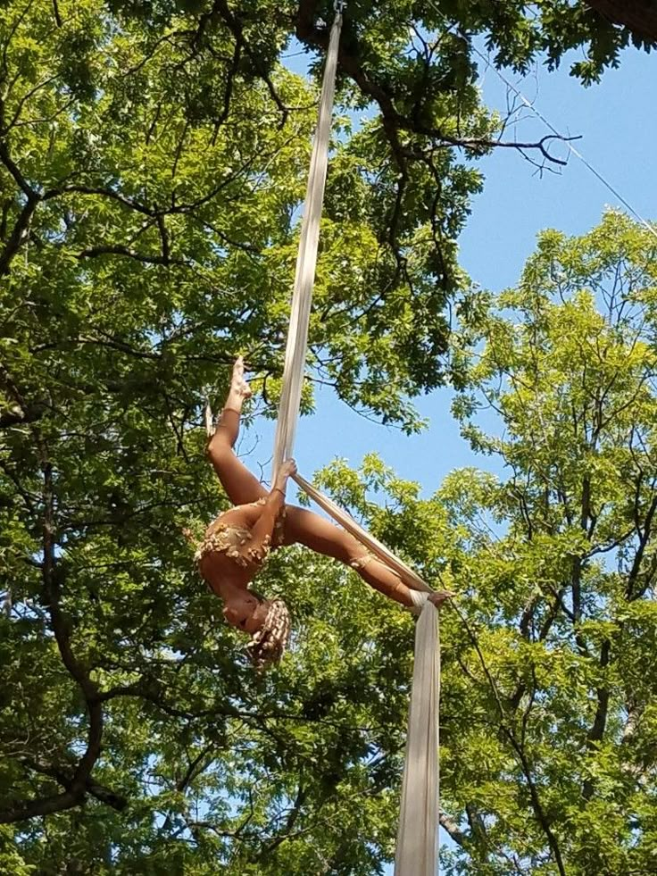 a woman is performing aerial acrobatic tricks on a pole in the woods