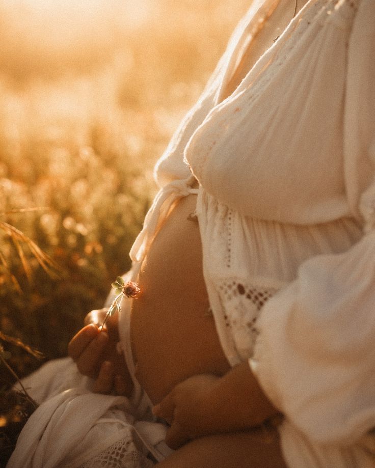 a pregnant woman is holding her belly in the grass with sunlight shining on her stomach