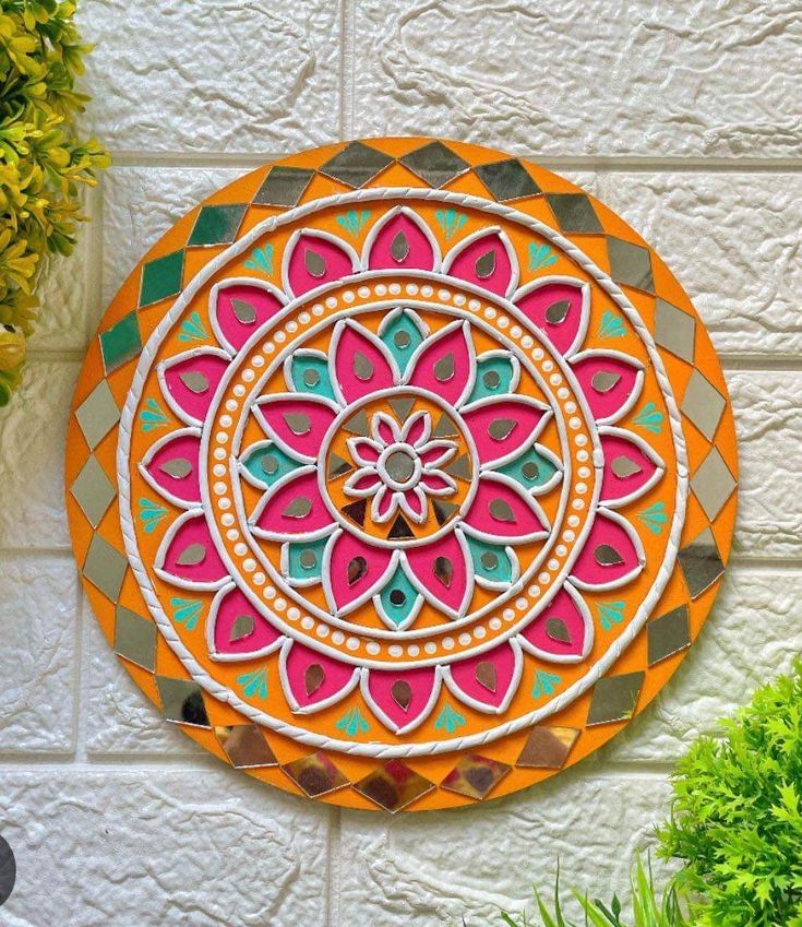 an orange and pink wall hanging on the side of a white brick building with potted plants