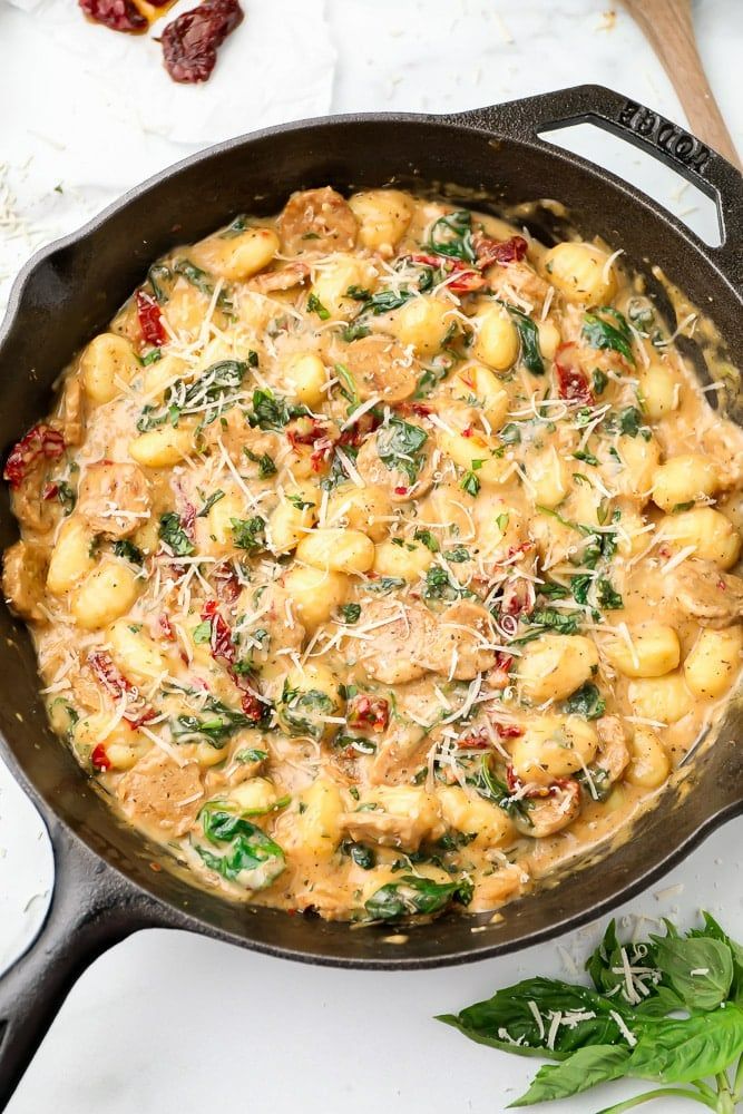 a skillet filled with pasta and spinach on top of a white countertop